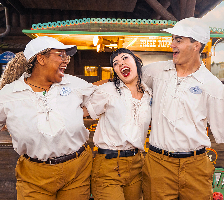3 young people in matching costumes, laughing together at a Disney park's Frontierland attraction