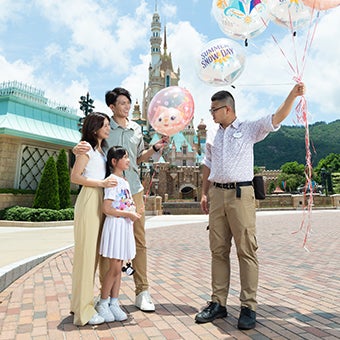 Disney College Program participant holding balloons while talking to a family at Hong Kong Disneyland